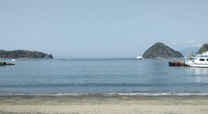 アニメで何度も登場した、内浦(うちうら)三津(みと)海水浴場(沼津市)。左側が長井崎、右側があわしま(淡島)。そして淡島の右側が、雲で隠れているが富士山。海の向こう側は、興津や清水のあたり。